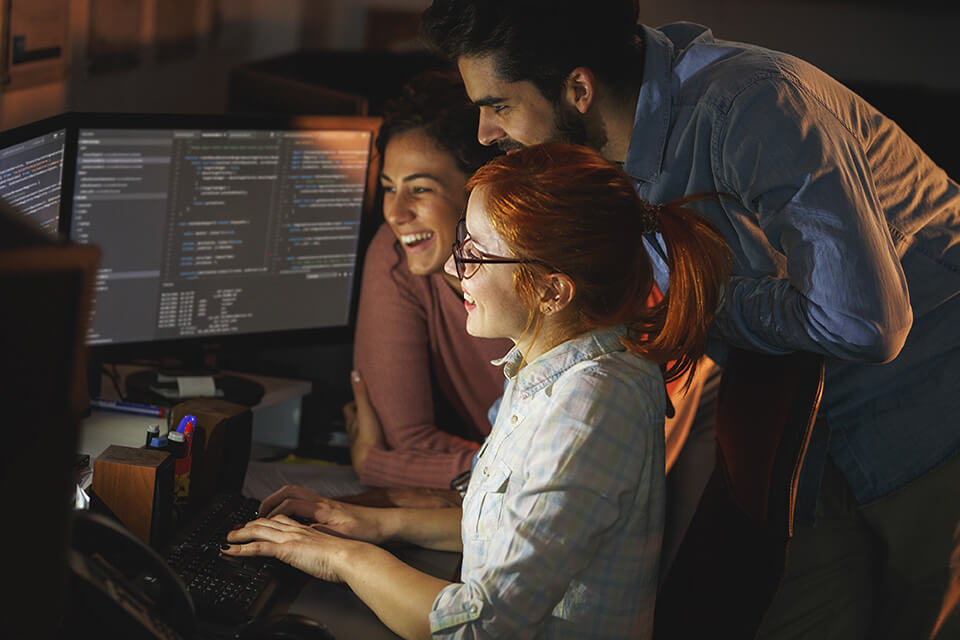 Stellenausschreibung-Software-Entwicklerin_mobile Drei Software-Entwickler*innen arbeiten gemeinsam im Büro an einem Computer mit zwei Bildschirmen.